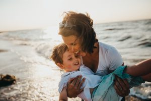 Eine Frau mit Kind am Meer. Unbeschwerter Urlaub sollte beim Immobilienkauf mit der cleveren Baufinanzierung für Alleinlebende möglich sein. 