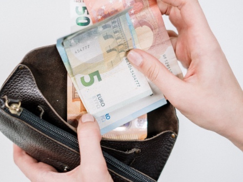 Eine Hand nimmt mehrere Euro-Scheine aus einem schwarzem Portemmonaie heraus, die andere Hand hält das Portemmonaie.