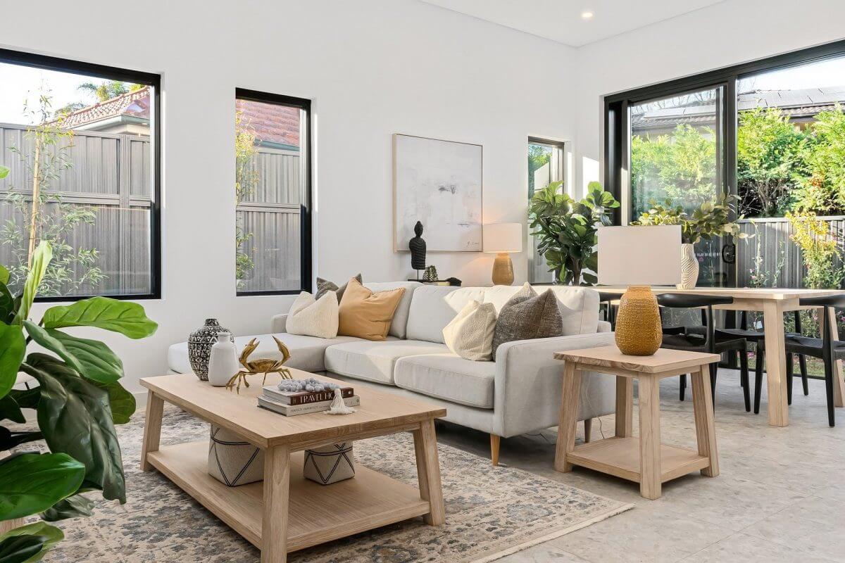 Ein möblierter Wohnbereich im Erdgeschoss mit mehreren Zimmerpflanzen. Im Garten befinden sich weitere Pflanzen und graue Sichtschutzwände.