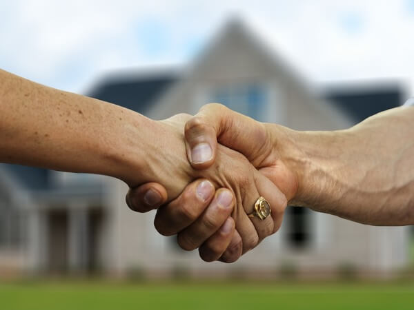 Handschlag und Immobilie im Hintergrund