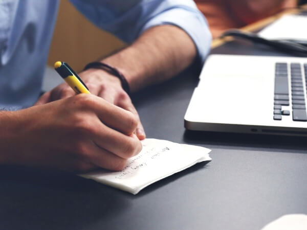Mann schreibt mit Stift auf Papierblock