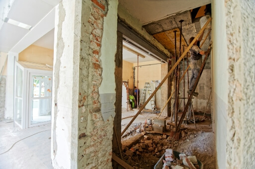 Ein baufälliger Altbau wird saniert. Holzgerüste stützen marode Wände, auf dem Boden liegt Holzschutt. 