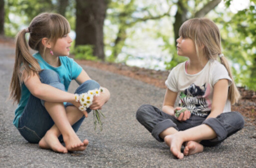 Zwei Mädchen sitzen auf dem Boden und unterhalten sich. 