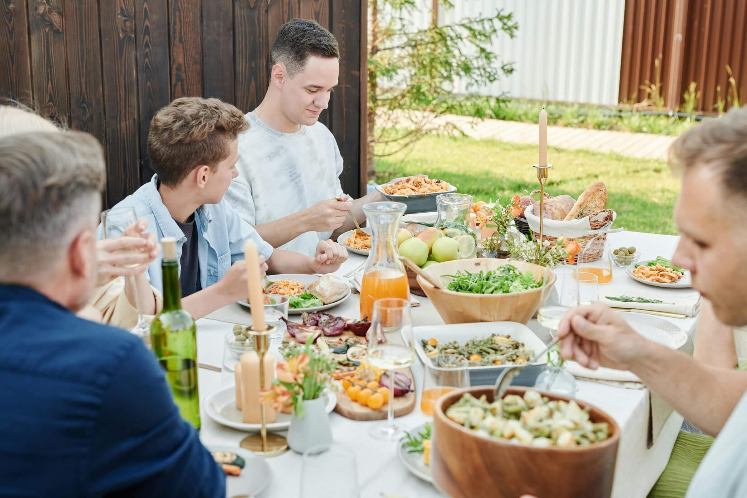 Junge Leute sitzen am Gartentisch und essen verschiedene Salate.