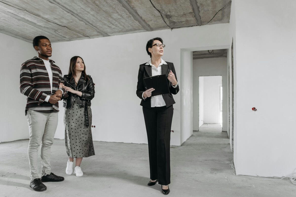 Ein junges Paar besichtigt mit einer Maklerin eine Wohnung im Rohbau.