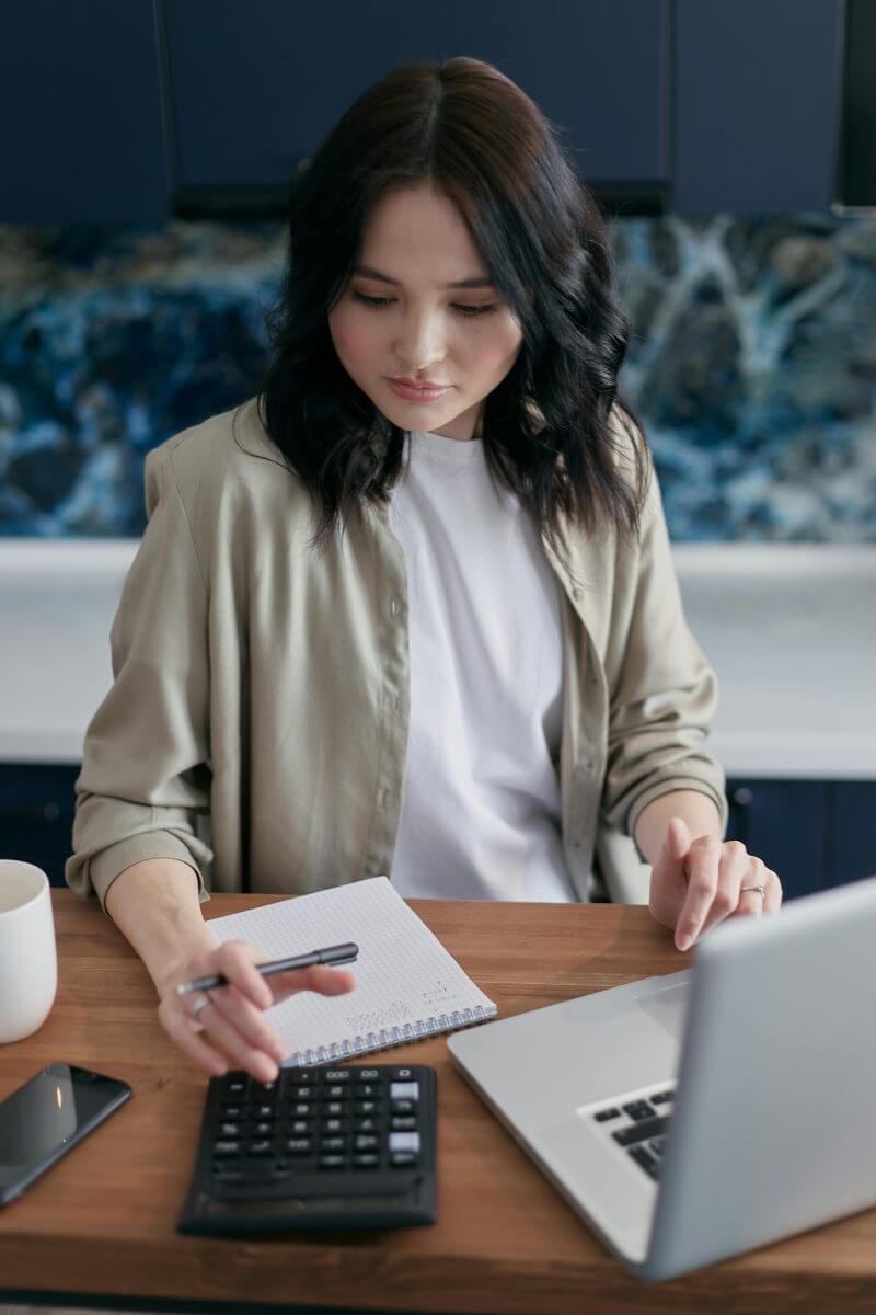 Frau kalkuliert Kosten mit Taschenrechner und Laptop