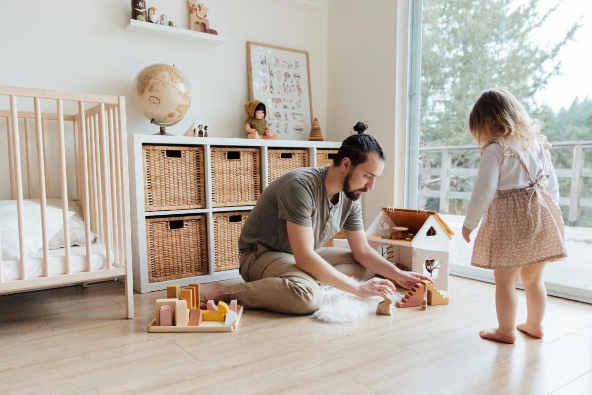 Vater spielt mit Kleinkind im Kinderzimmer mit Holzspielzeug. 