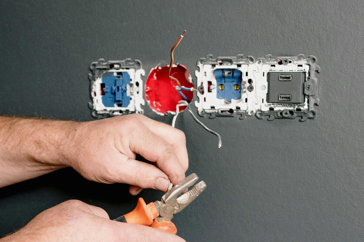 Person hält Stromkabel mit einer Zange bei der Installation einer Unterputzdose.
